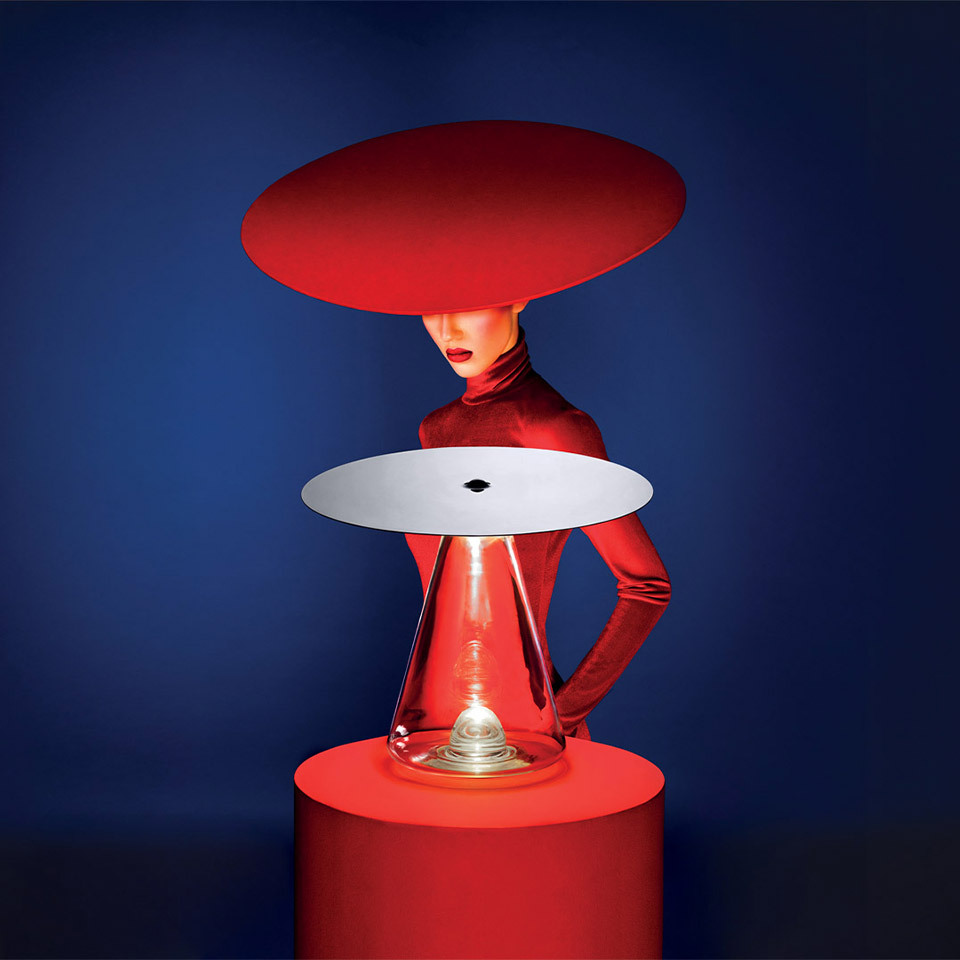 Artemide Boltons table lamp: red conical glass base with white reflective disc shade, styled with a model in red outfit against blue background