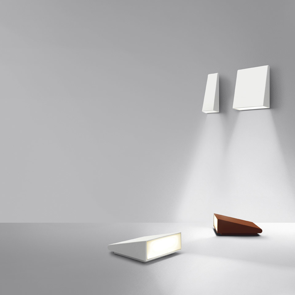 Collezione Artemide Cuneo: due applique bianche con fasci di luce verso il basso, più lampade da terra a cuneo in bianco e finitura legno