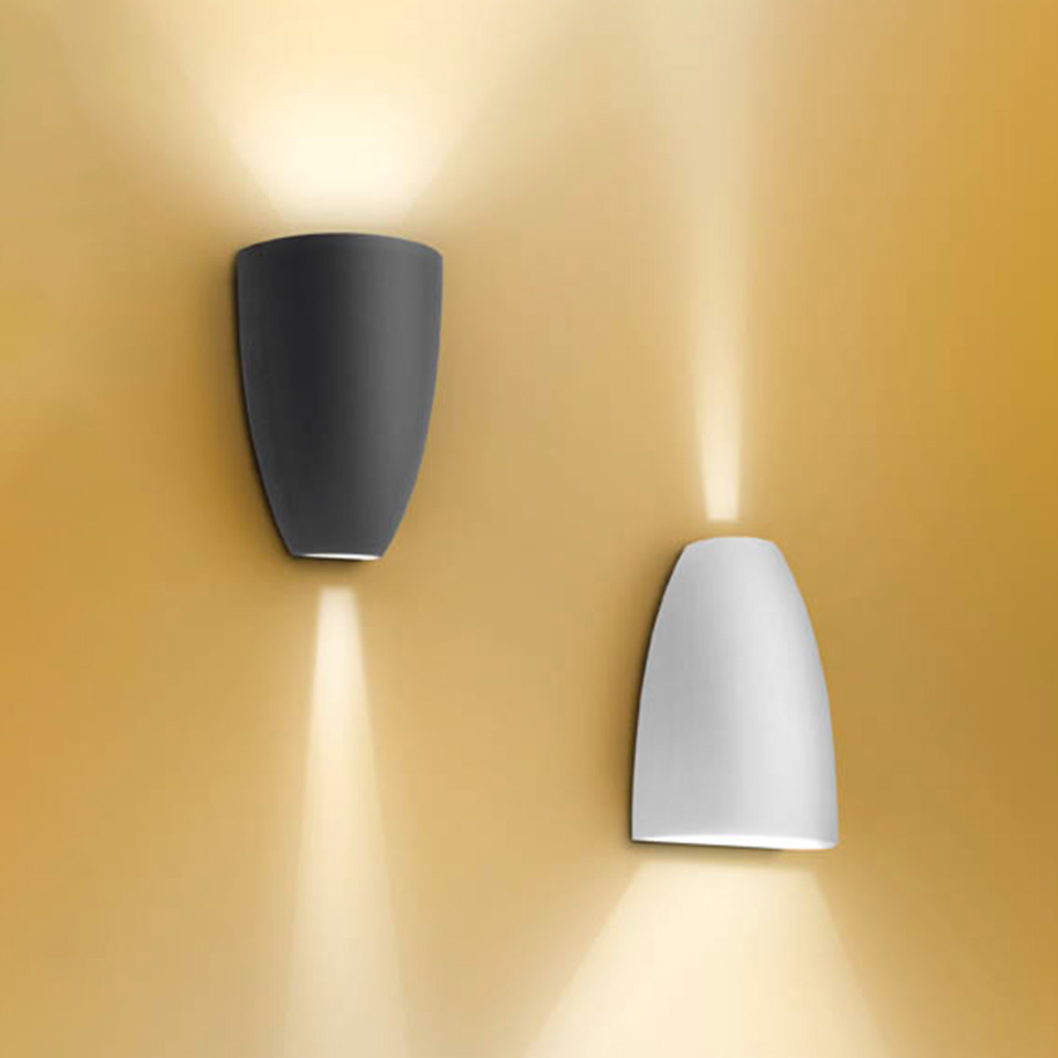Applique da parete Artemide Molla in antracite e bianco, con fasci di luce calda verso l'alto e il basso su parete dorata