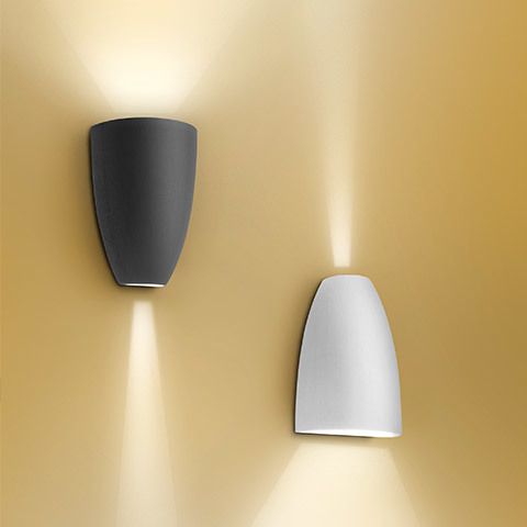 Applique da parete Artemide Molla in antracite e bianco, con fasci di luce calda verso l'alto e il basso su parete dorata