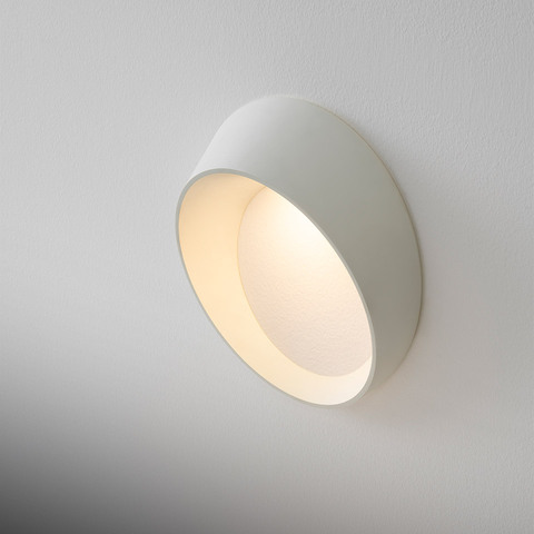 Applique da parete Artemide Cleomede bianca con paralume circolare inclinato che emette luce calda e diffusa su parete bianca