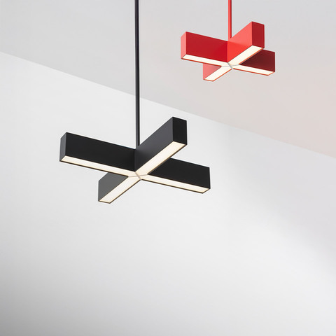 Two Artemide Tetras pendant lamps in cross shape: larger black version in foreground, smaller red version in background, both emitting LED light