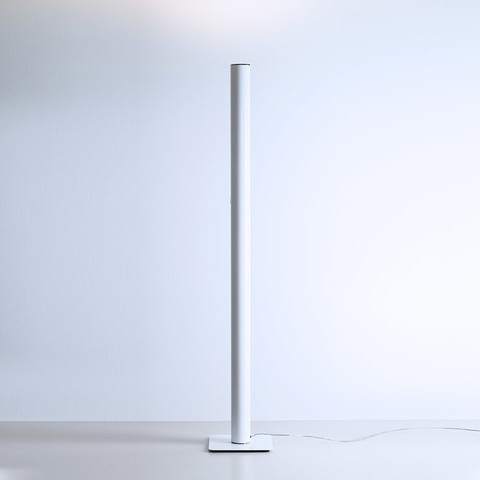 Artemide Ilio INTEGRALIS floor lamp: slim white cylindrical column on square base, emitting upward indirect light
