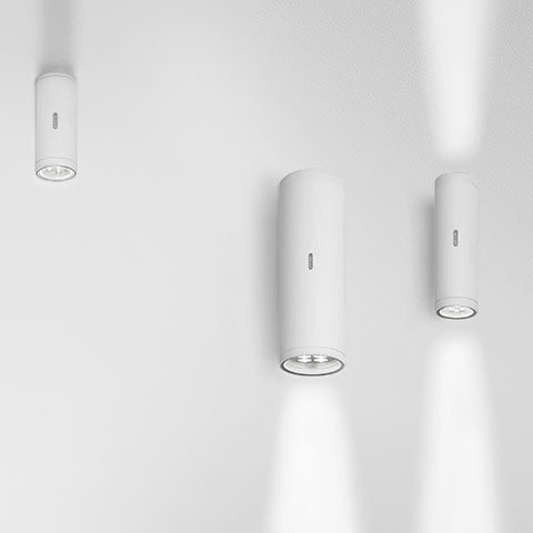 Tre faretti da soffitto cilindrici bianchi Artemide Calumet di diverse dimensioni, ognuno con un fascio di luce diretto verso il basso.