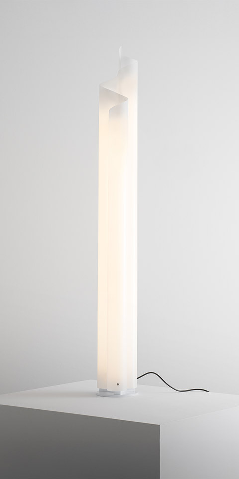 Artemide Chimera floor lamp: tall white sculptural column diffuser emitting soft warm light, with black power cord