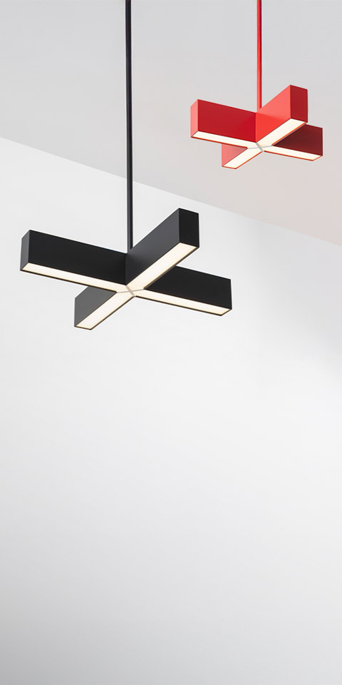 Two Artemide Tetras pendant lamps in cross shape: larger black version in foreground, smaller red version in background, both emitting LED light