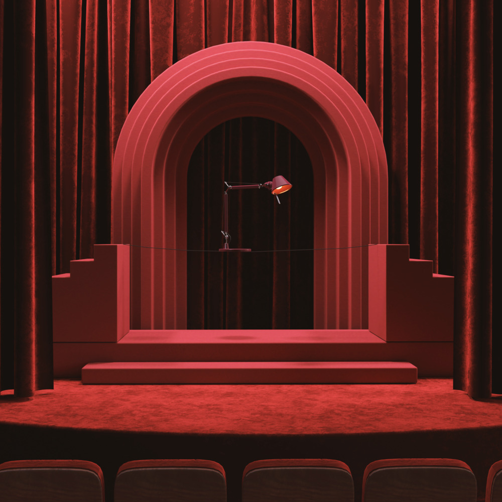 Artemide desk lamp on a red theatrical stage with arched backdrop and velvet curtains, dramatic monochromatic red setting