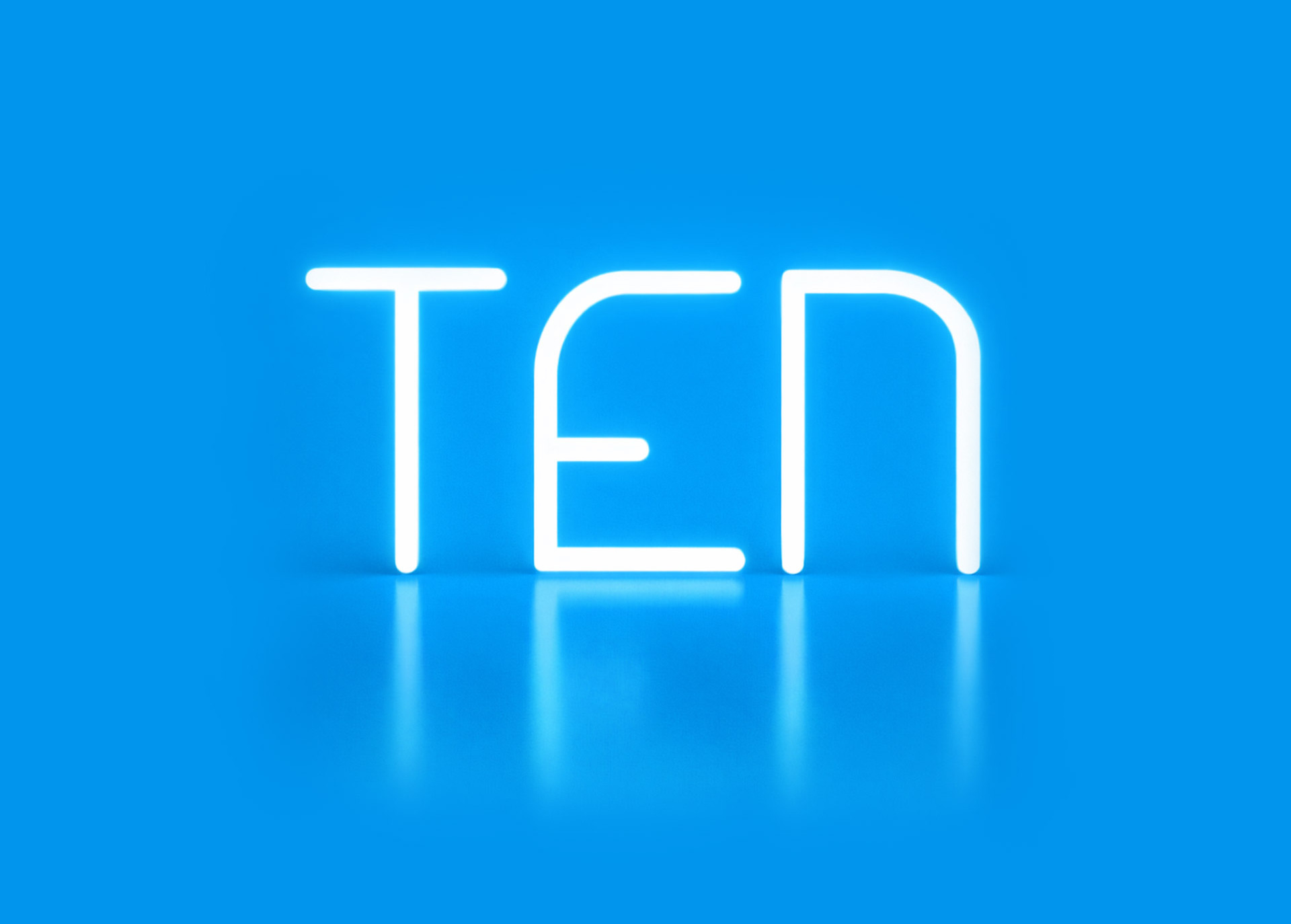 Scritta luminosa “TEN” realizzata con Alphabet of Light, su sfondo azzurro con riflesso sulla superficie lucida.
