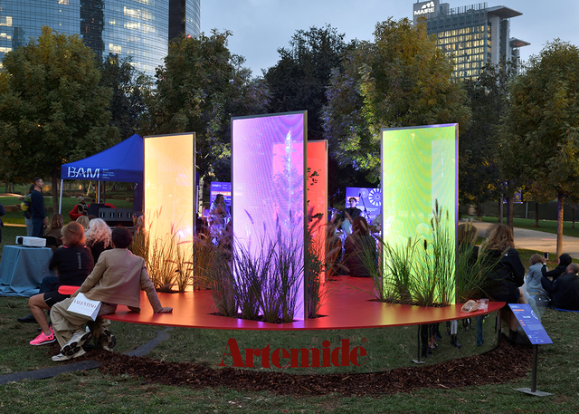 Artemide outdoor installation with illuminated colorful vertical panels in purple, red, and green, surrounded by ornamental grasses at dusk.