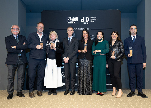 Carlotta de Bevilacqua posa insieme agli altri premiati durante la Italian Design Week 2026 a Washington, davanti al pannello ufficiale dell’evento.
