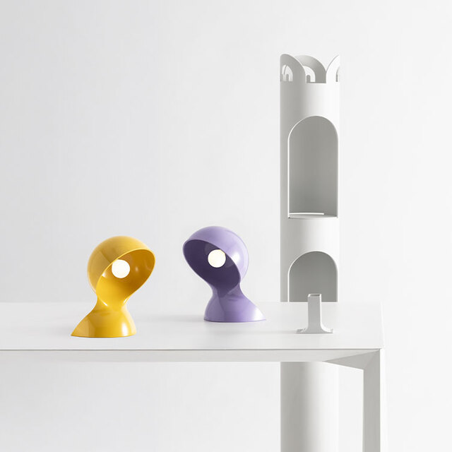 Composizione su tavolo bianco con due lampade Dalù nei colori lilla e giallo su sfondo chiaro.