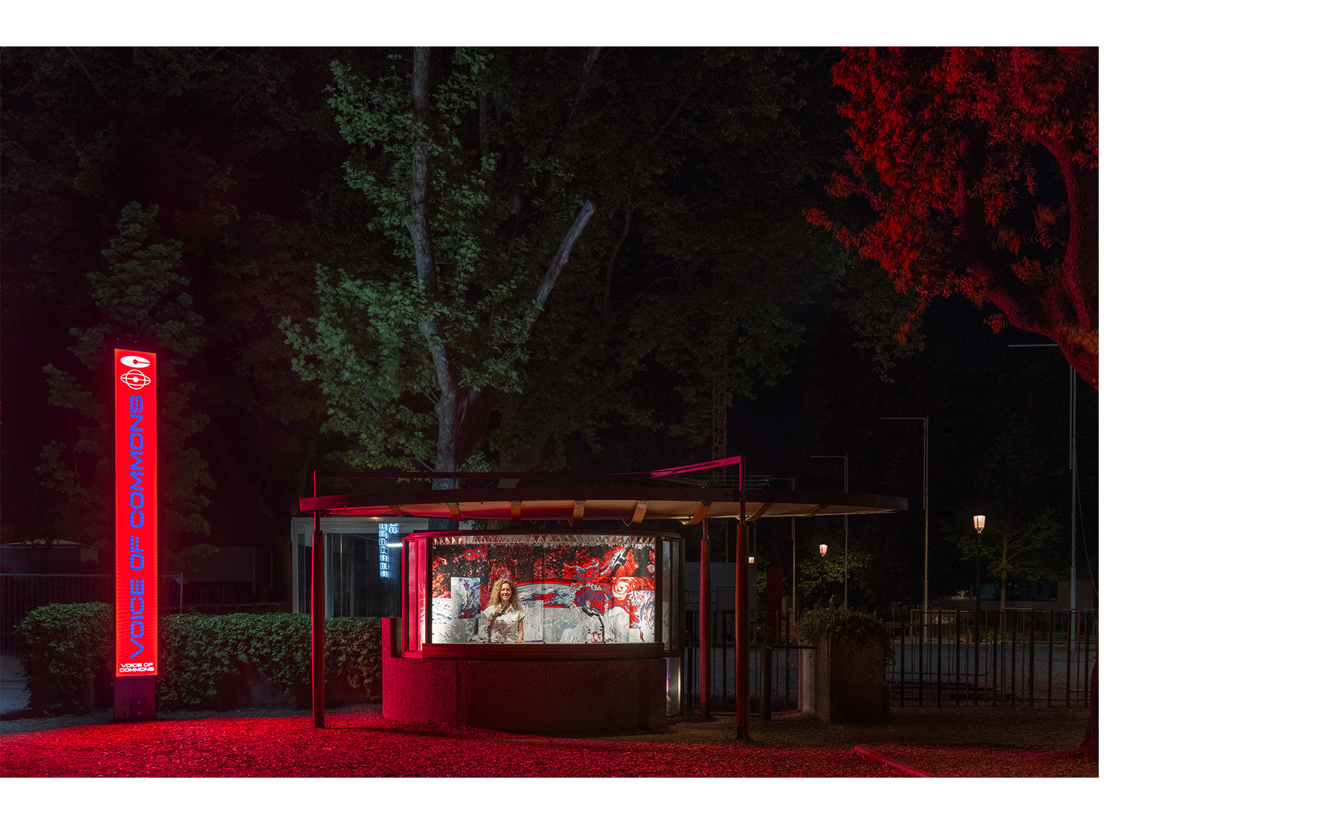 Chiosco esterno illuminato in rosso di notte con vetrina illuminata, insegna al neon e alberi drammaticamente illuminati in rosso