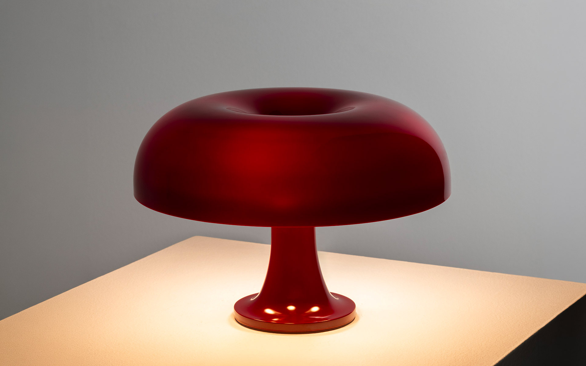 Lampada Nessino bordeaux accesa su piedistallo bianco.