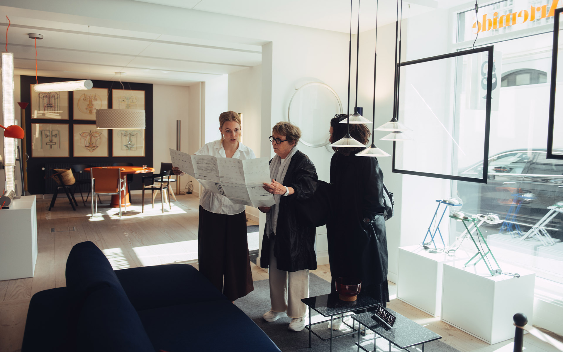 Tre persone che consultano documenti in uno showroom Artemide, con lampade a sospensione e esposizioni di illuminazione sullo sfondo.