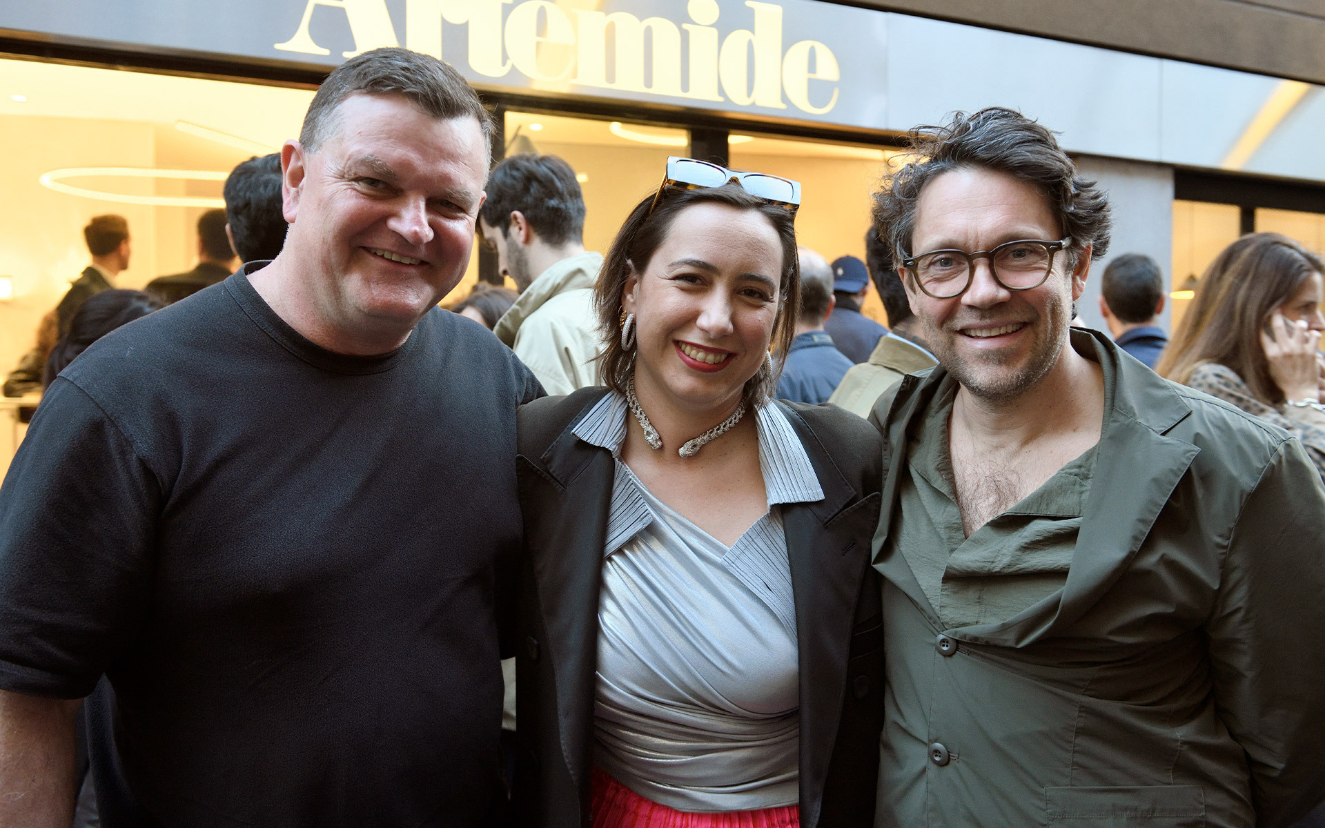 Tre persone che sorridono insieme davanti all'ingresso di un negozio Artemide durante un evento.