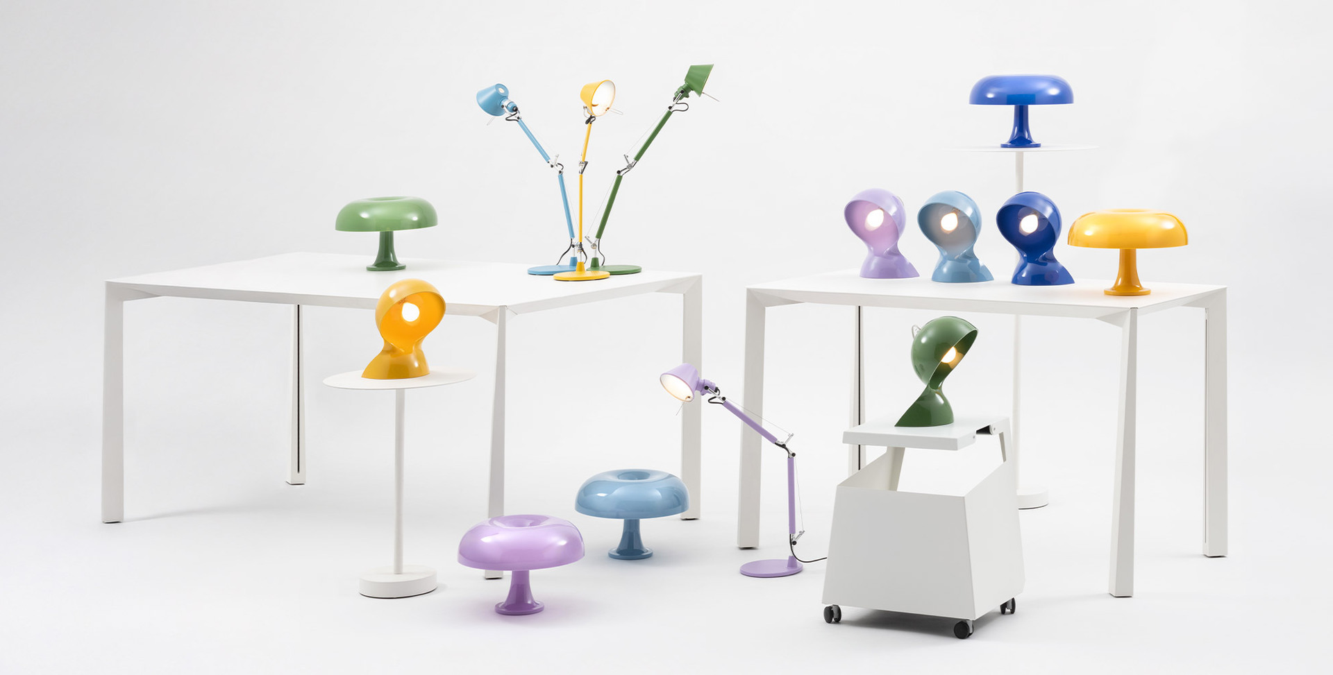 Composizione di lampade Dalù, Nessino e Tolomeo in vari colori, disposte su tavoli bianchi con sfondo neutro.