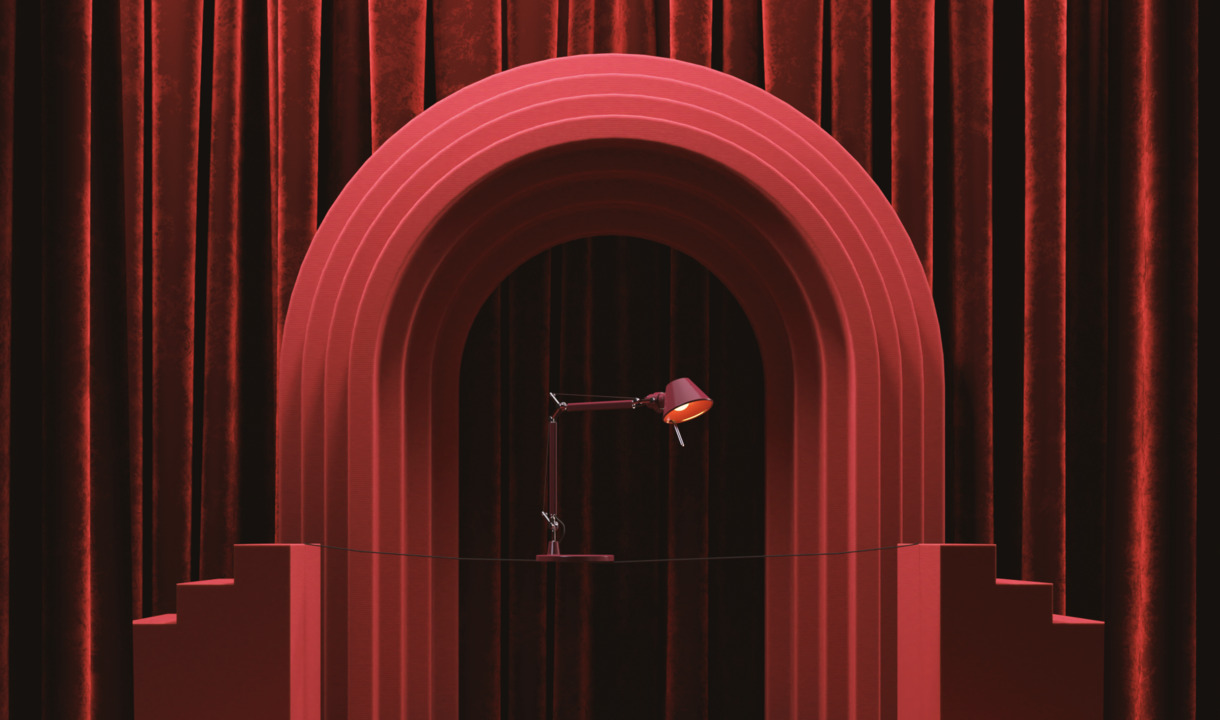 Lampada da tavolo Tolomeo Micro bordeaux esposta su un palcoscenico con arco scenografico e tende in velluto.