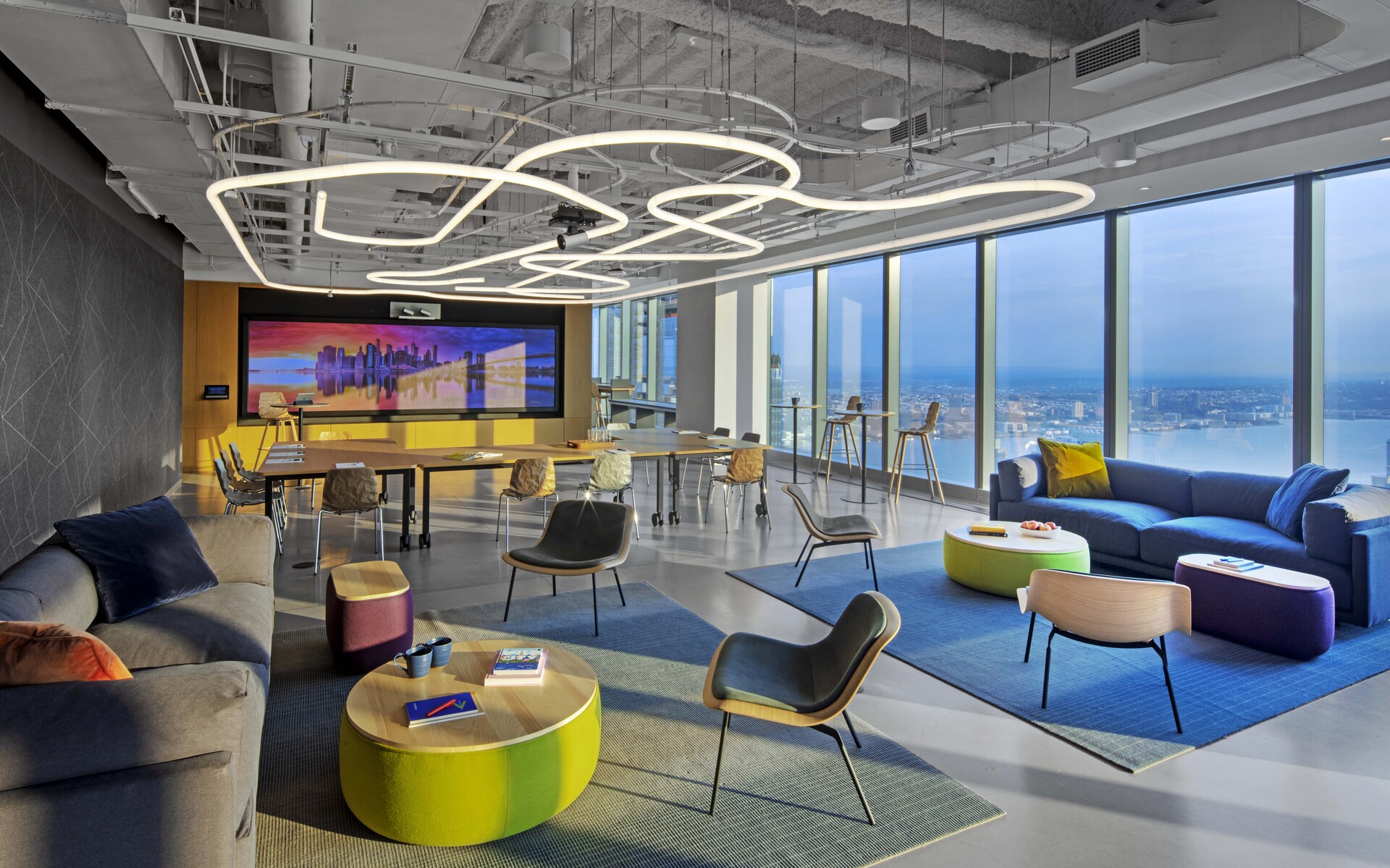 Lounge ufficio moderno con lampade a sospensione Artemide ad anelli interconnessi, mobili colorati e vista panoramica sulla città.