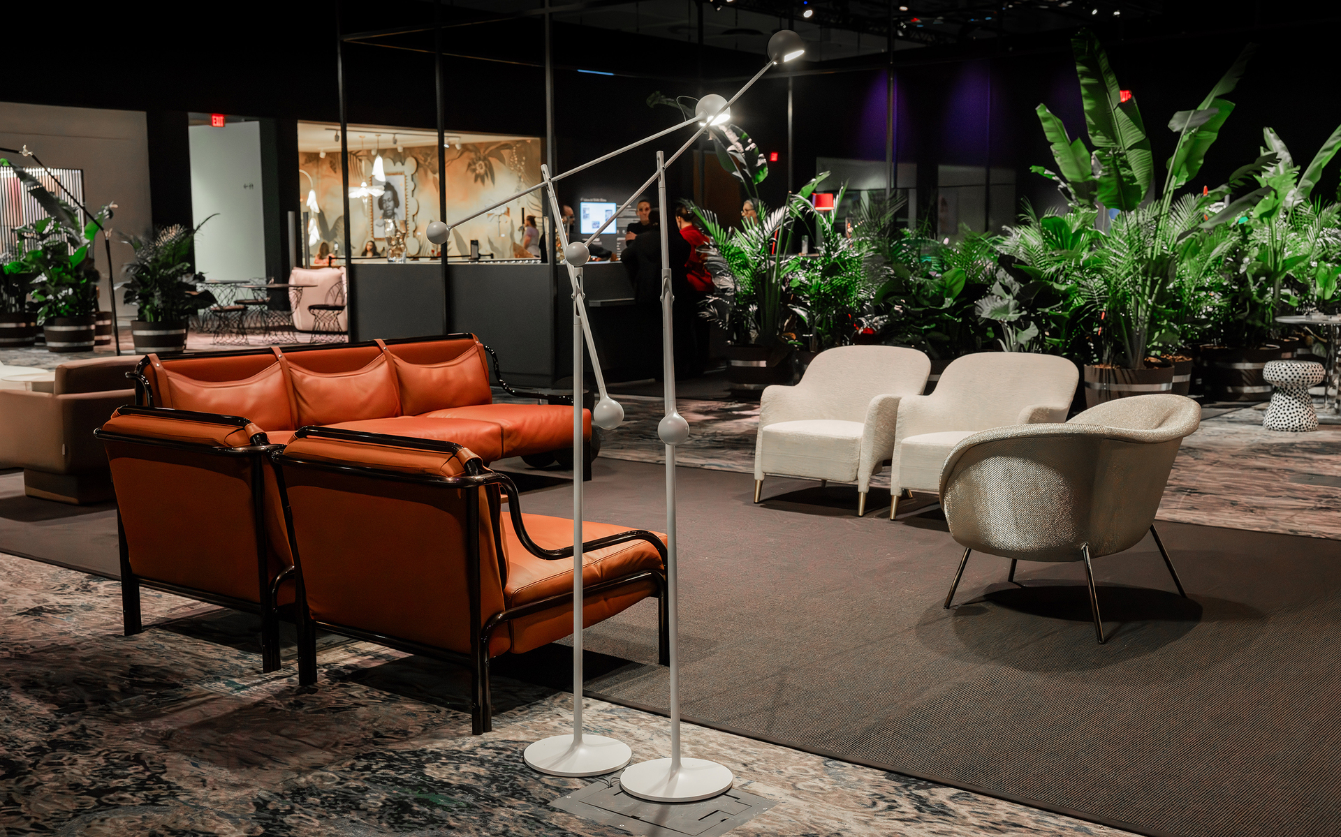 Lampada da terra Artemide con braccio regolabile in uno showroom, accanto a divani in pelle e poltrone bianche tra rigogliosa vegetazione.