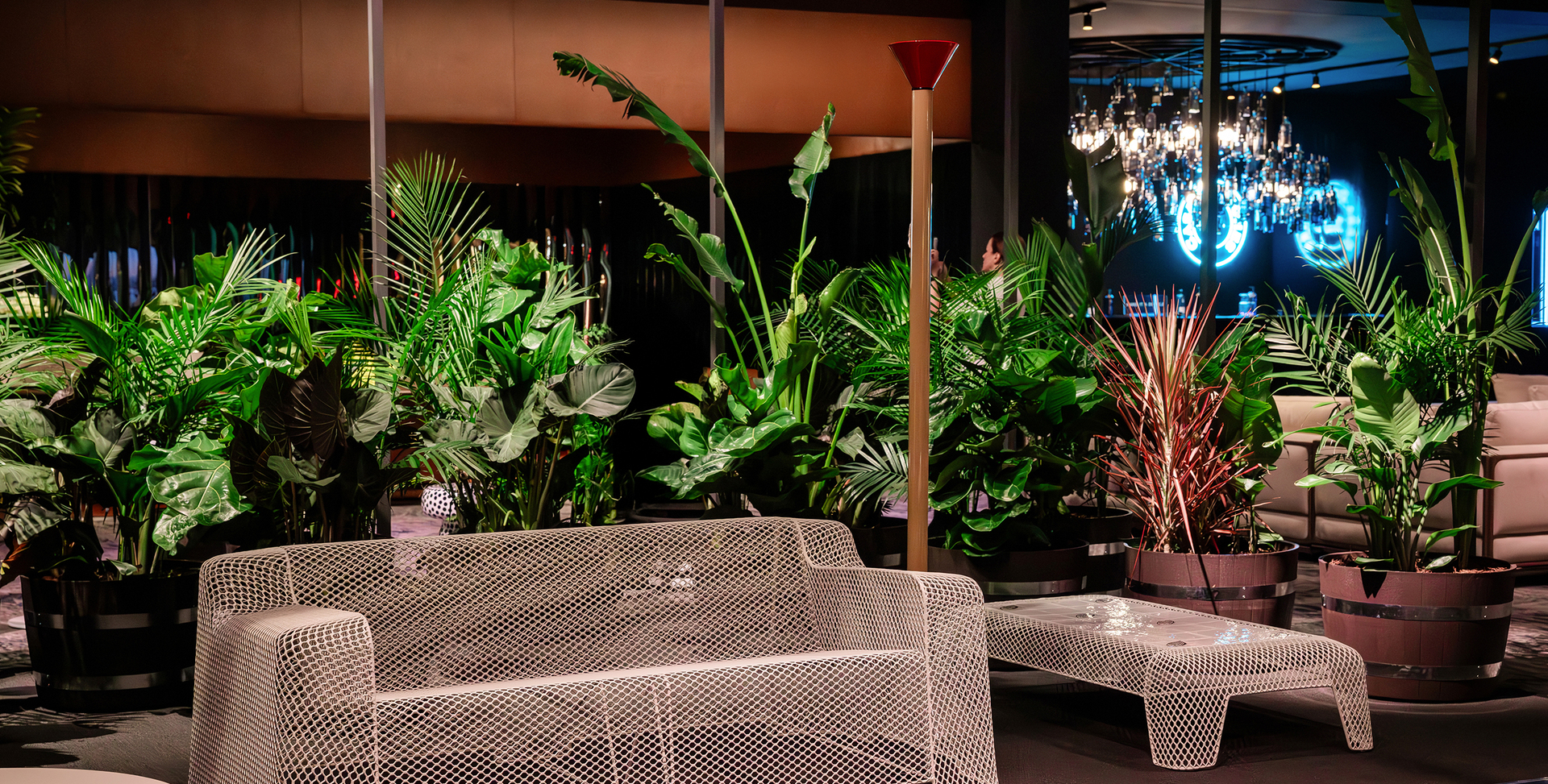 Allestimento della Collectors Lounge del Salone del Mobile.Milano ad Art Basel Miami Beach, con area living composta da divano, tavolino laterale e lampada Callimaco di Artemide; sullo sfondo, elementi vegetali definiscono lo spazio.