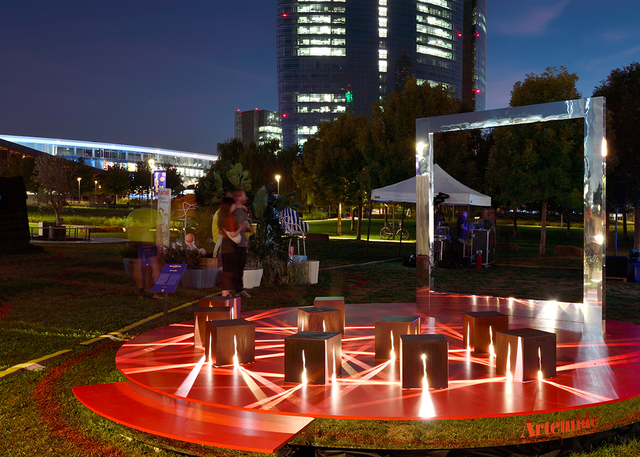 Installazione luminosa con cubi e fasci di luce rossa in parco urbano notturno.