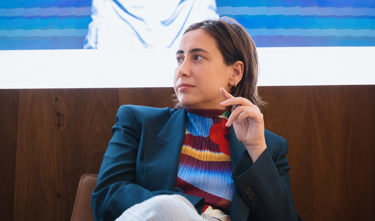 Carolina Gismondi de Bevilacqua seated during a talk, looking towards another speaker.