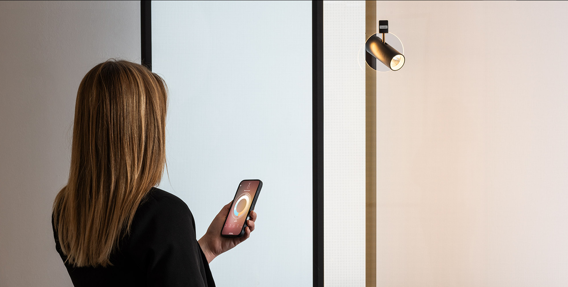 Donna controlla un faretto a parete tramite app su smartphone.