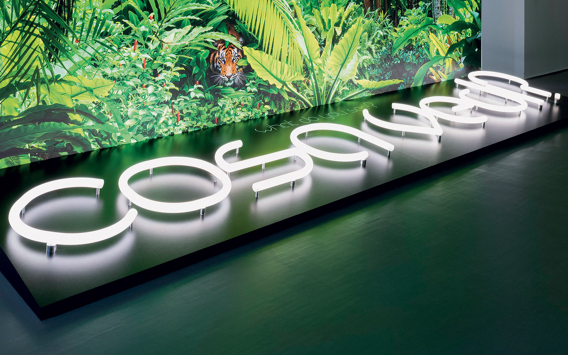 Lettere al neon bianche illuminate che formano 'cosmo' su una base scura, con uno sfondo di giungla tropicale lussureggiante con una tigre.