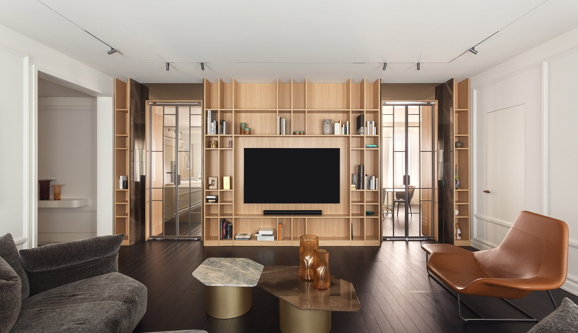 Soggiorno con libreria in legno, TV e illuminazione a binario a soffitto.