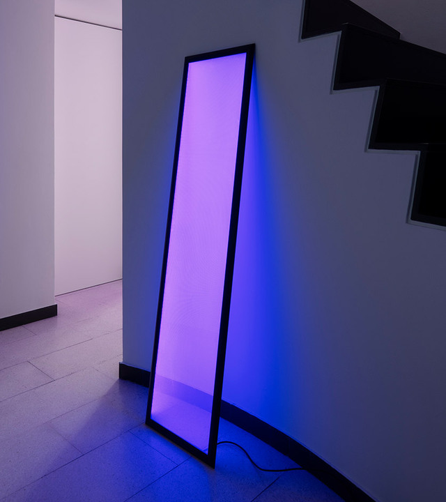 Pannello luminoso verticale con luce viola appoggiato a parete.
