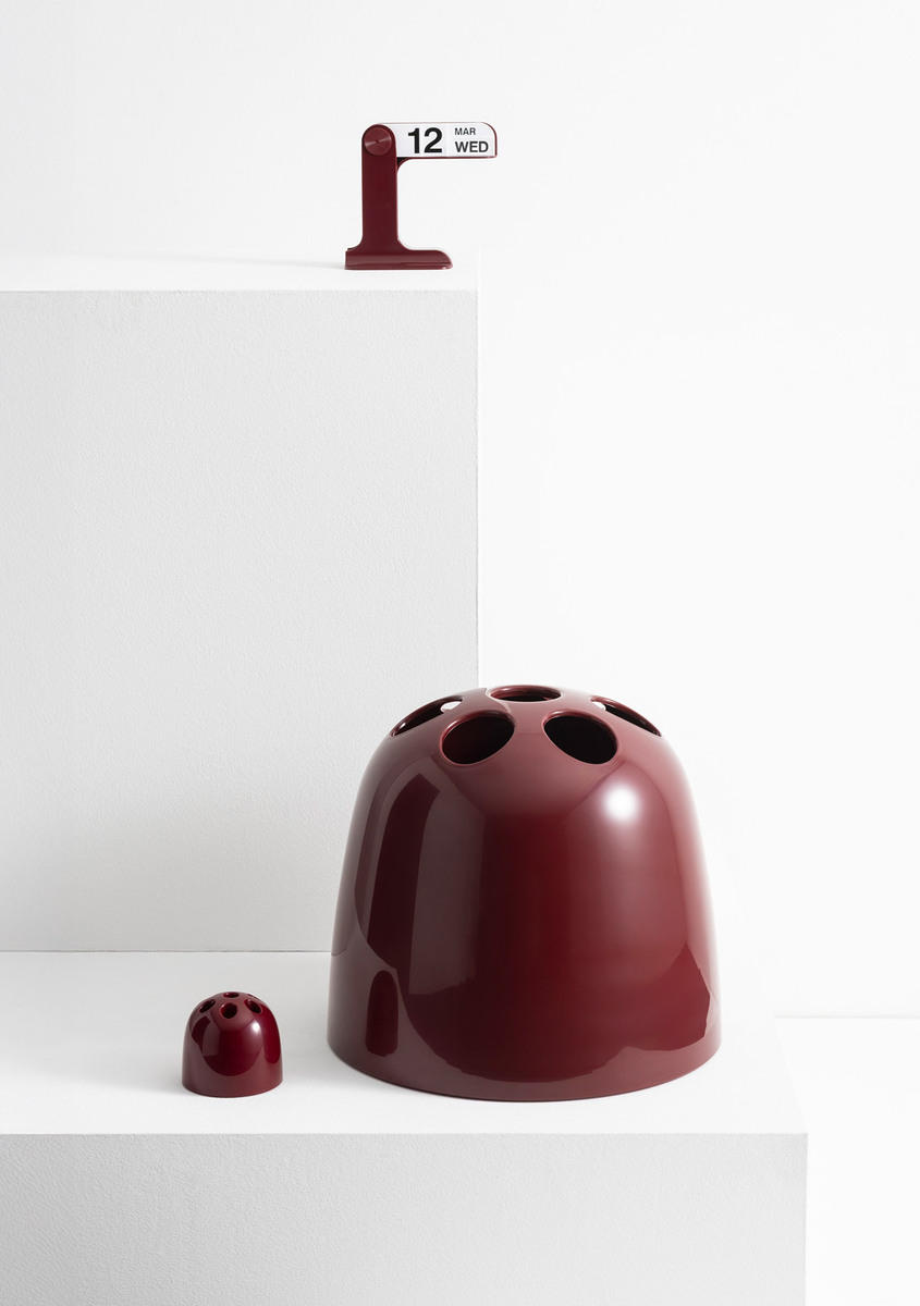 Composizione di oggetti di design Danese Milano bordeaux su piedistalli bianchi.