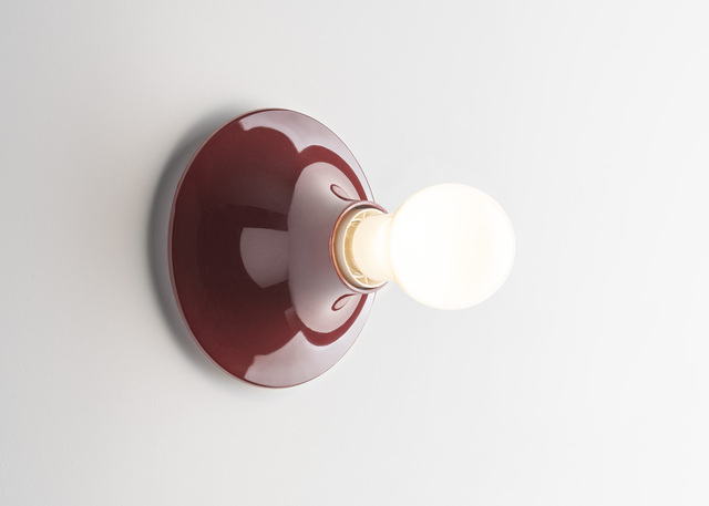 Lampada da parete Teti bordeaux con lampadina sferica accesa, montata su una parete bianca.