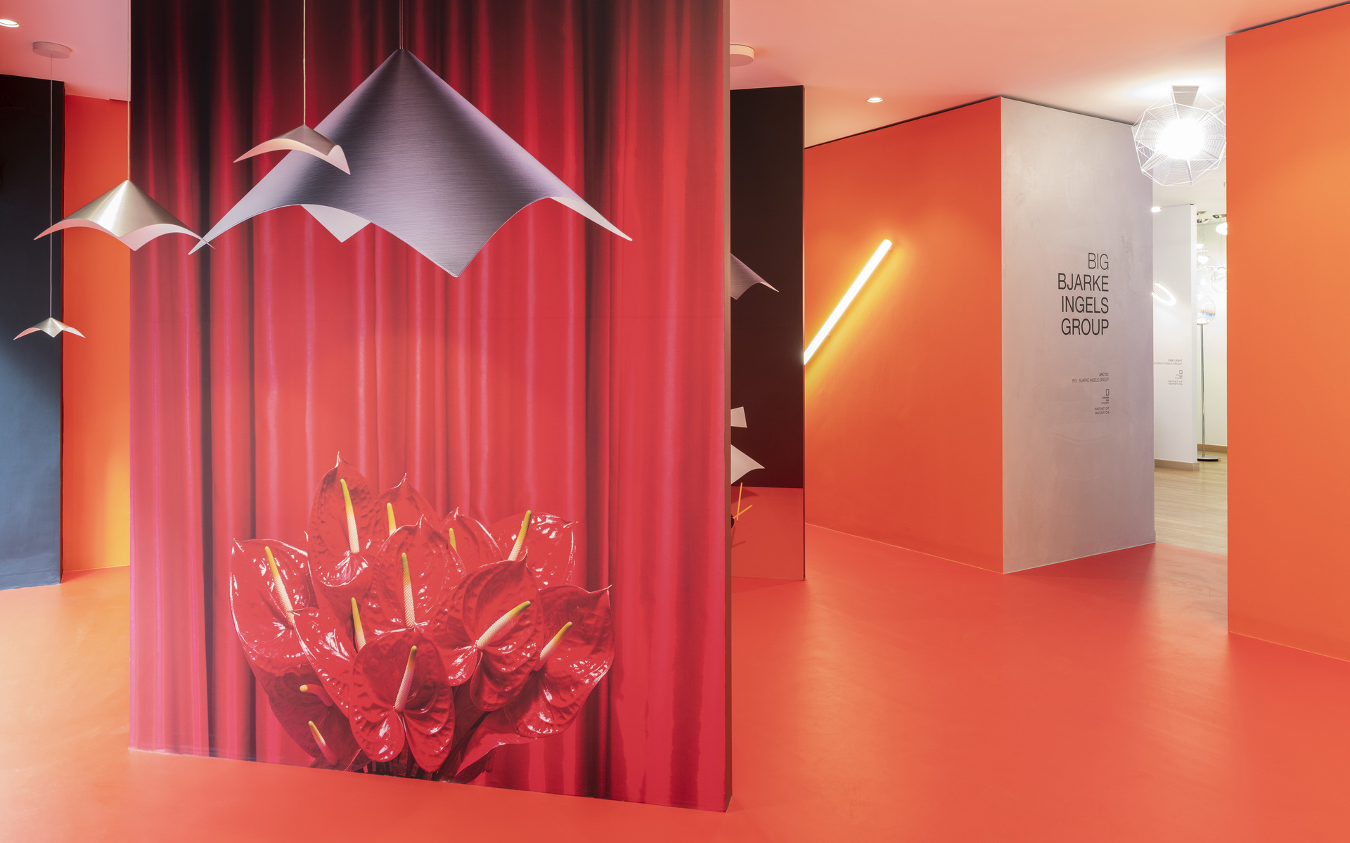 Ufficio BIG Bjarke Ingels Group con lampade a sospensione Artemide a forma origami e lampada lineare a parete in un corridoio arancione vivace