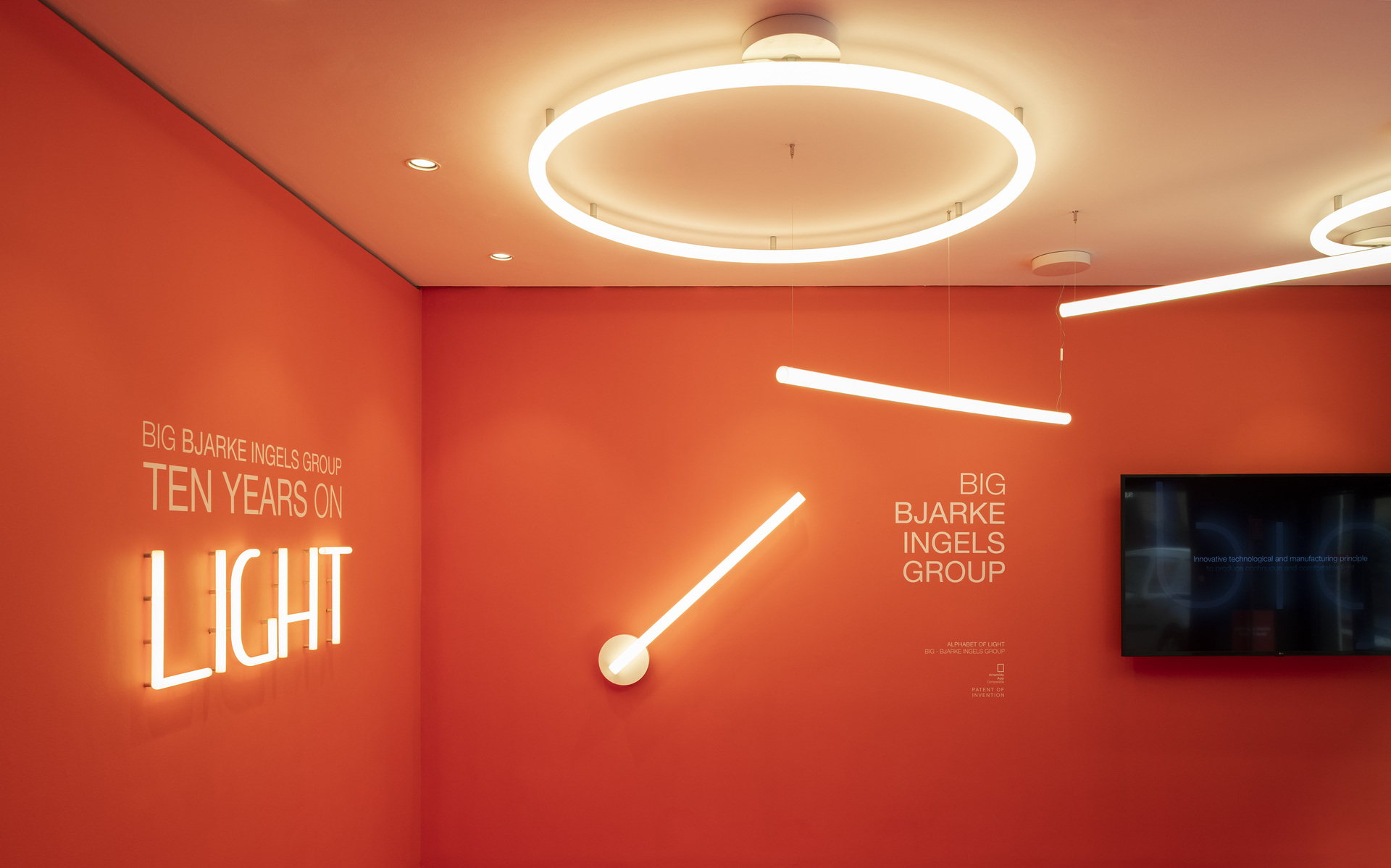 Mostra BIG Bjarke Ingels Group con luci al neon e plafoniera circolare LED Artemide su pareti arancioni, intitolata 'Ten Years on Light'