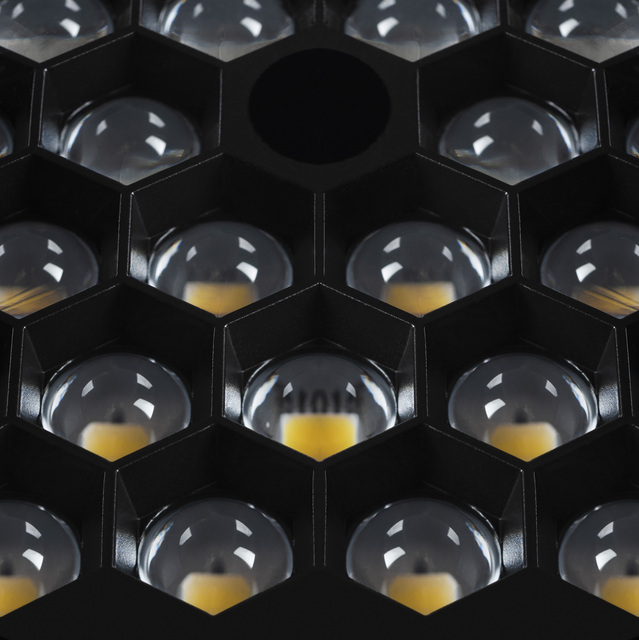 Primo piano di un pannello LED nero a nido d'ape con celle esagonali multiple, ciascuna con una lente a cupola trasparente su una sorgente LED caldo.