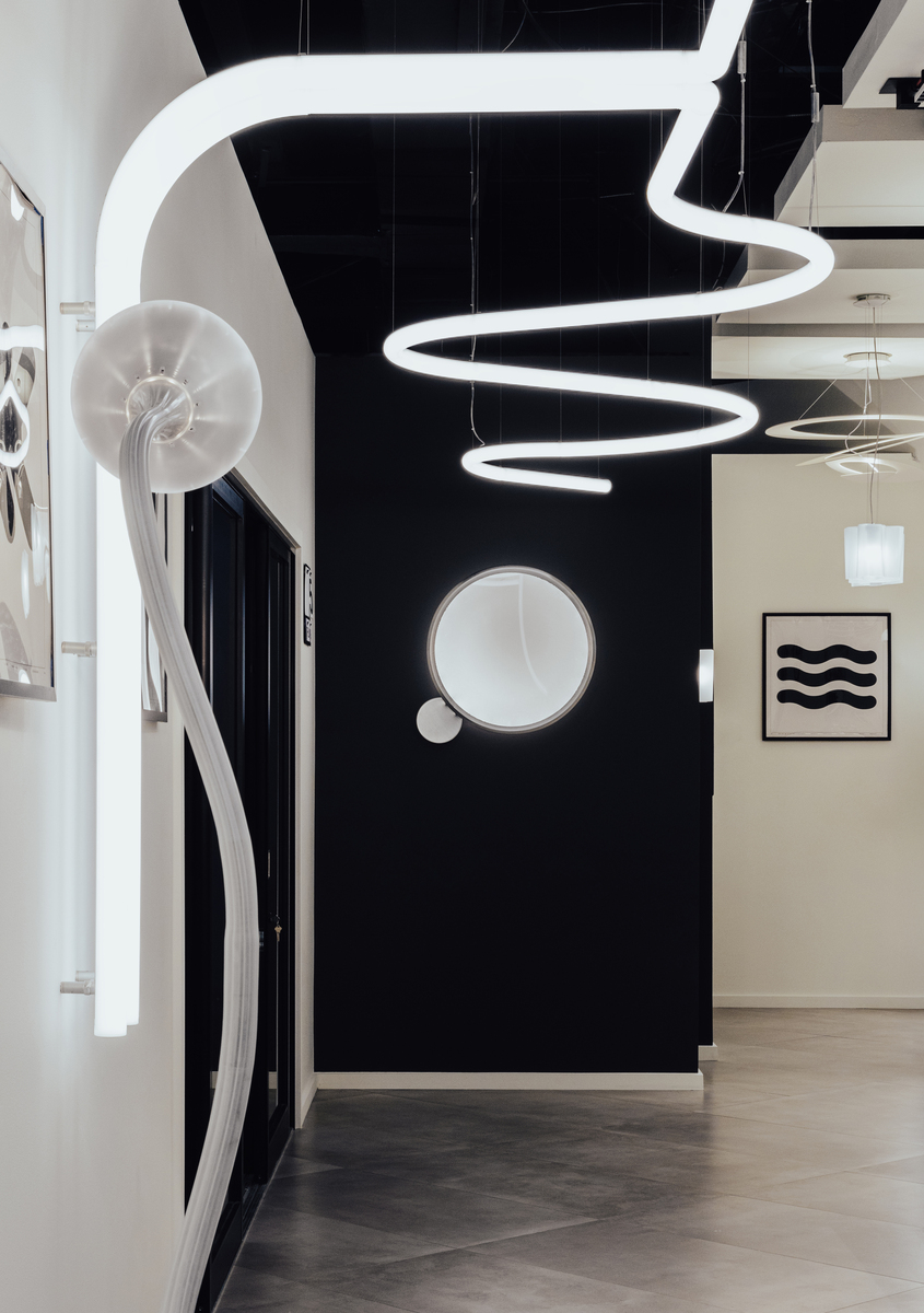 Showroom Artemide con lampada a sospensione spirale su soffitto nero, applique circolare a parete e applique a conchiglia su arco bianco