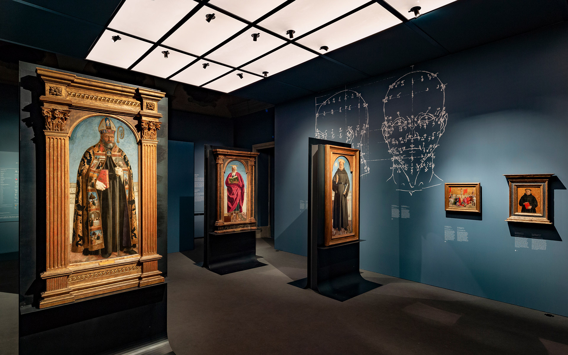Galleria museale con dipinti rinascimentali su pareti verde acqua scuro, illuminata da faretti a soffitto Artemide su sistema a binario a griglia.
