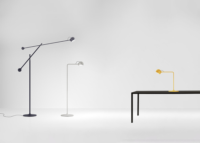 Tre lampade Artemide: lampada da terra articolata scura, lampada da lettura bianca e lampada da tavolo gialla su tavolo nero