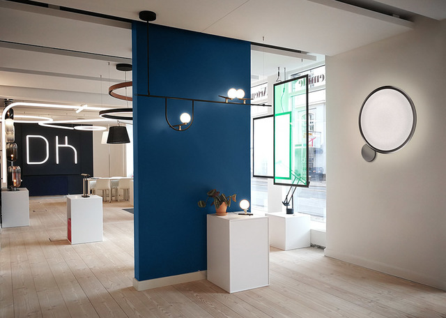Showroom Artemide con lampada a sospensione con bulbi sferici, grande applique rotonda e lampade da tavolo su piedistalli bianchi.