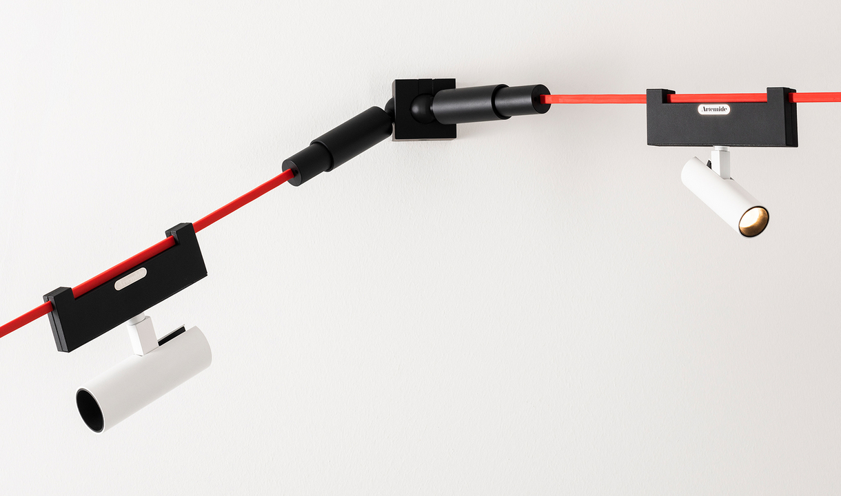 Sistema di illuminazione su binario Artemide con cavo rosso, connettori neri e due faretti cilindrici bianchi orientabili a soffitto