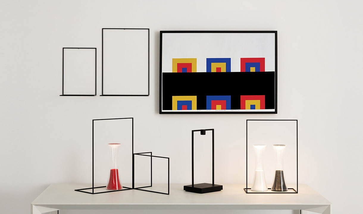 Tre lampade da tavolo Artemide con strutture minimaliste in filo nero su superficie bianca, con paralumi conici rosso, nero e bianco