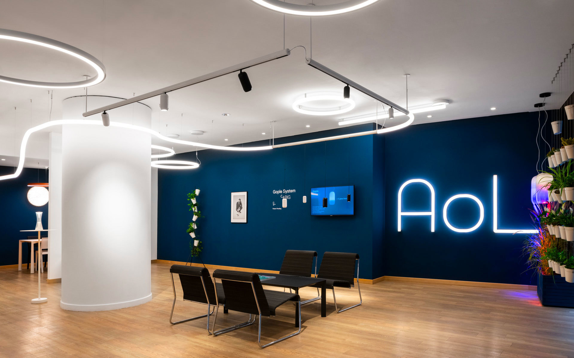 Ufficio AOL moderno con lampade a sospensione circolari LED e faretti su binario sopra un tavolo riunioni, su parete blu scuro con brand