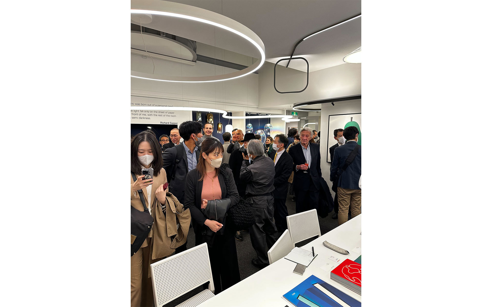 Guests mingle at an Artemide event beneath large circular LED pendant lights illuminating a modern showroom space.