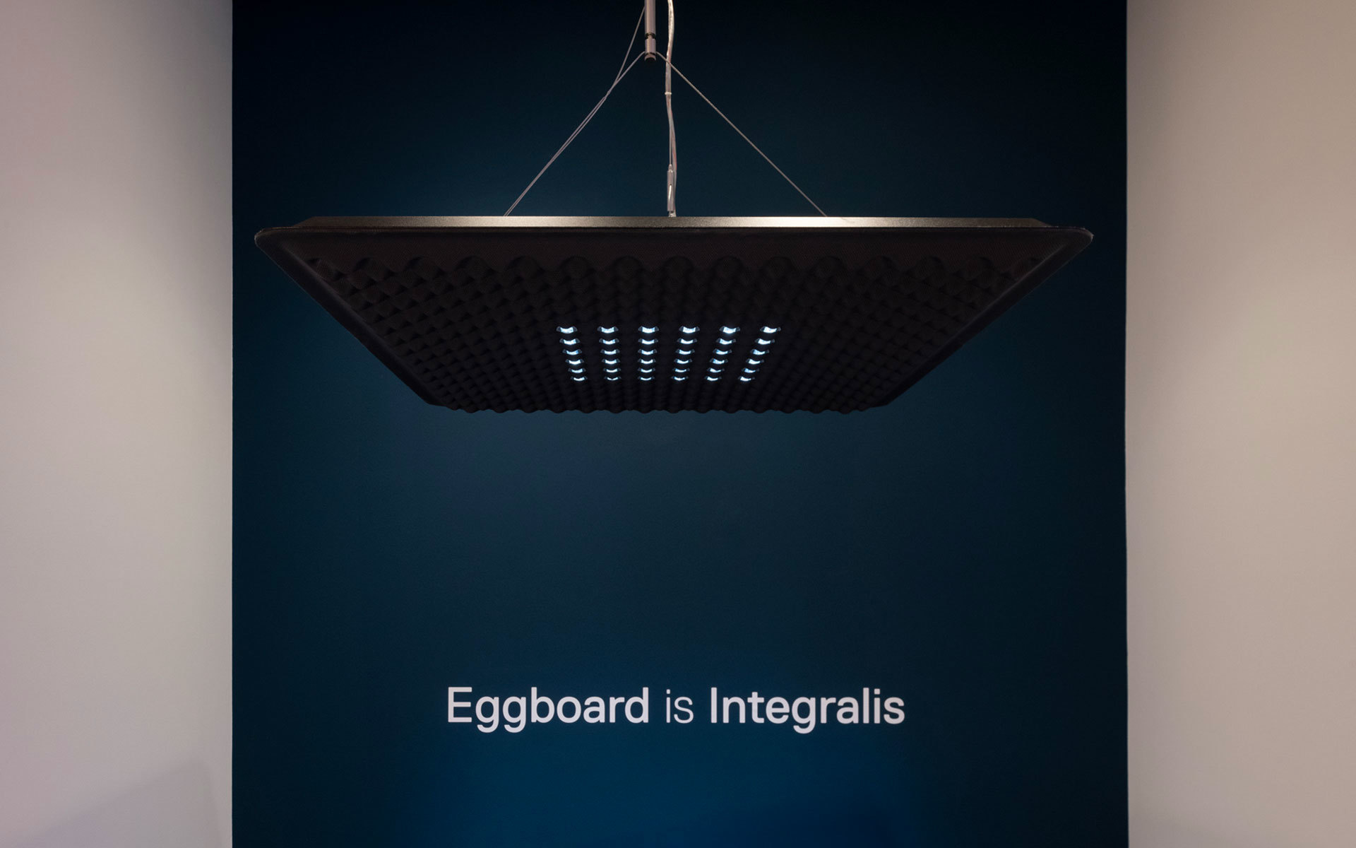 Lampada a sospensione Artemide Eggboard Integralis, paralume quadrato scuro con array LED, sospesa da cavi in acciaio su parete verde acqua
