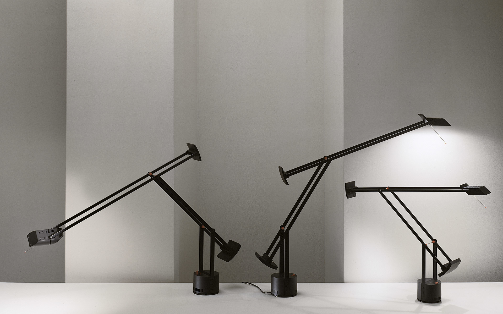 Two Artemide Tizio desk lamps in black with counterbalance arm design and circular bases, one tilted left, one right.