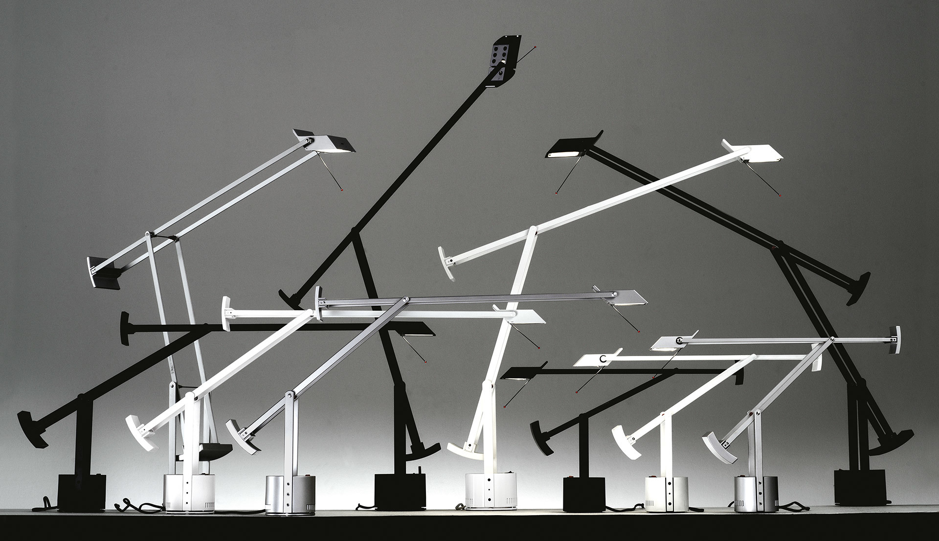 Collection of Artemide Tizio desk lamps in black and white, displayed in various positions showcasing their iconic adjustable arm design.