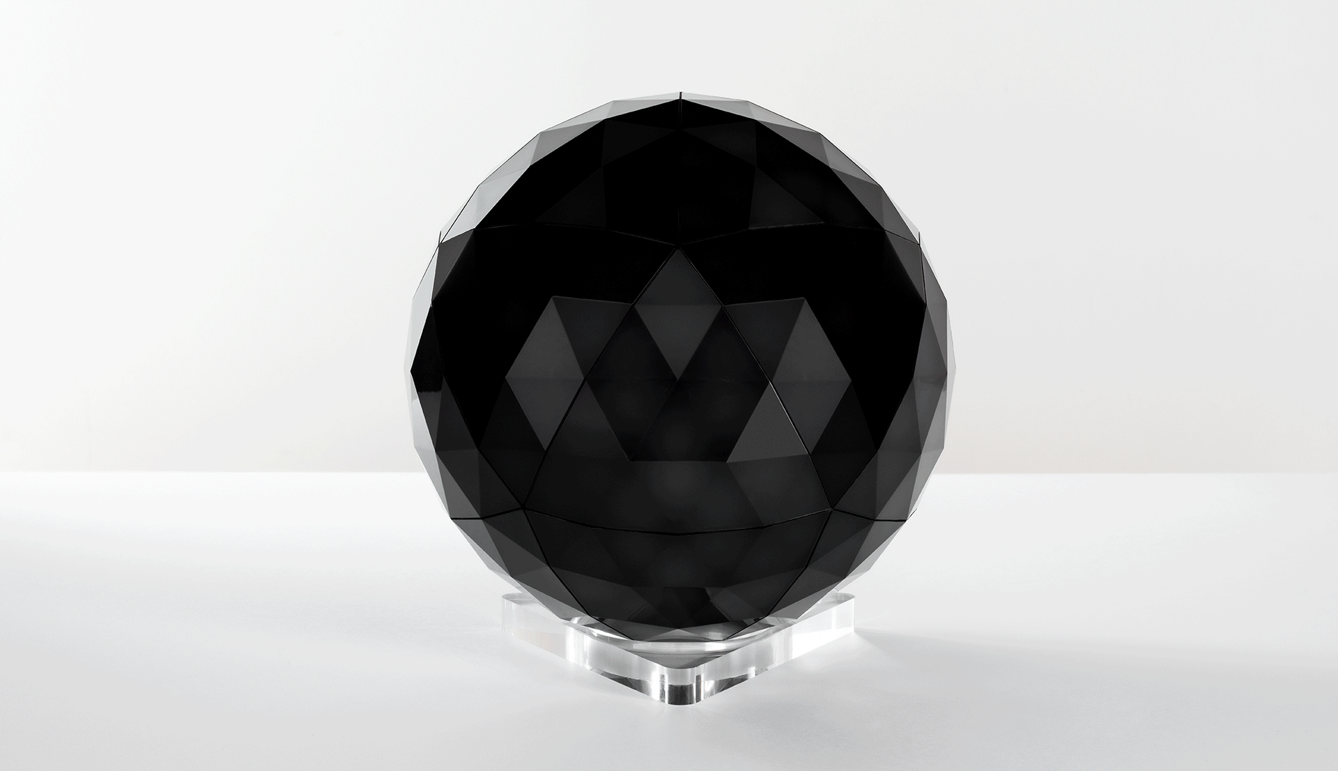 Lampada da tavolo sferica Artemide con struttura metallica triangolare geodetica che diffonde luce bianca soffusa, montata su base in cristallo trasparente