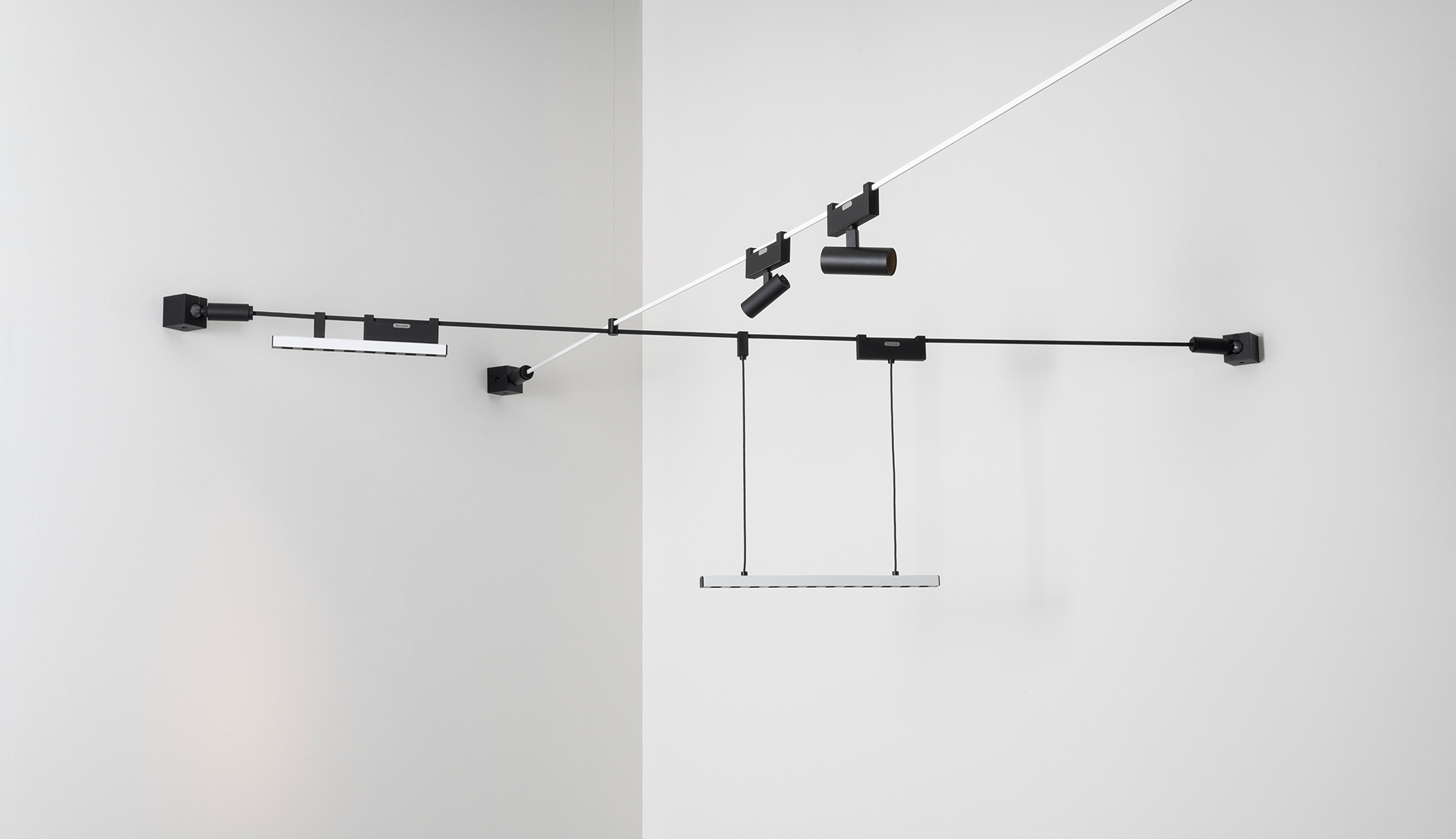 Sistema di illuminazione su binario nero Artemide montato su pareti bianche, con faretti, barra LED lineare a sospensione ed elementi a cavo