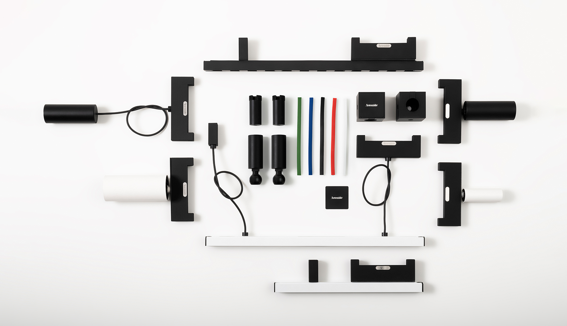 Componenti di sistema illuminotecnico Artemide disposti in piano: elementi modulari neri e bianchi, connettori, cavi e aste colorate su sfondo bianco