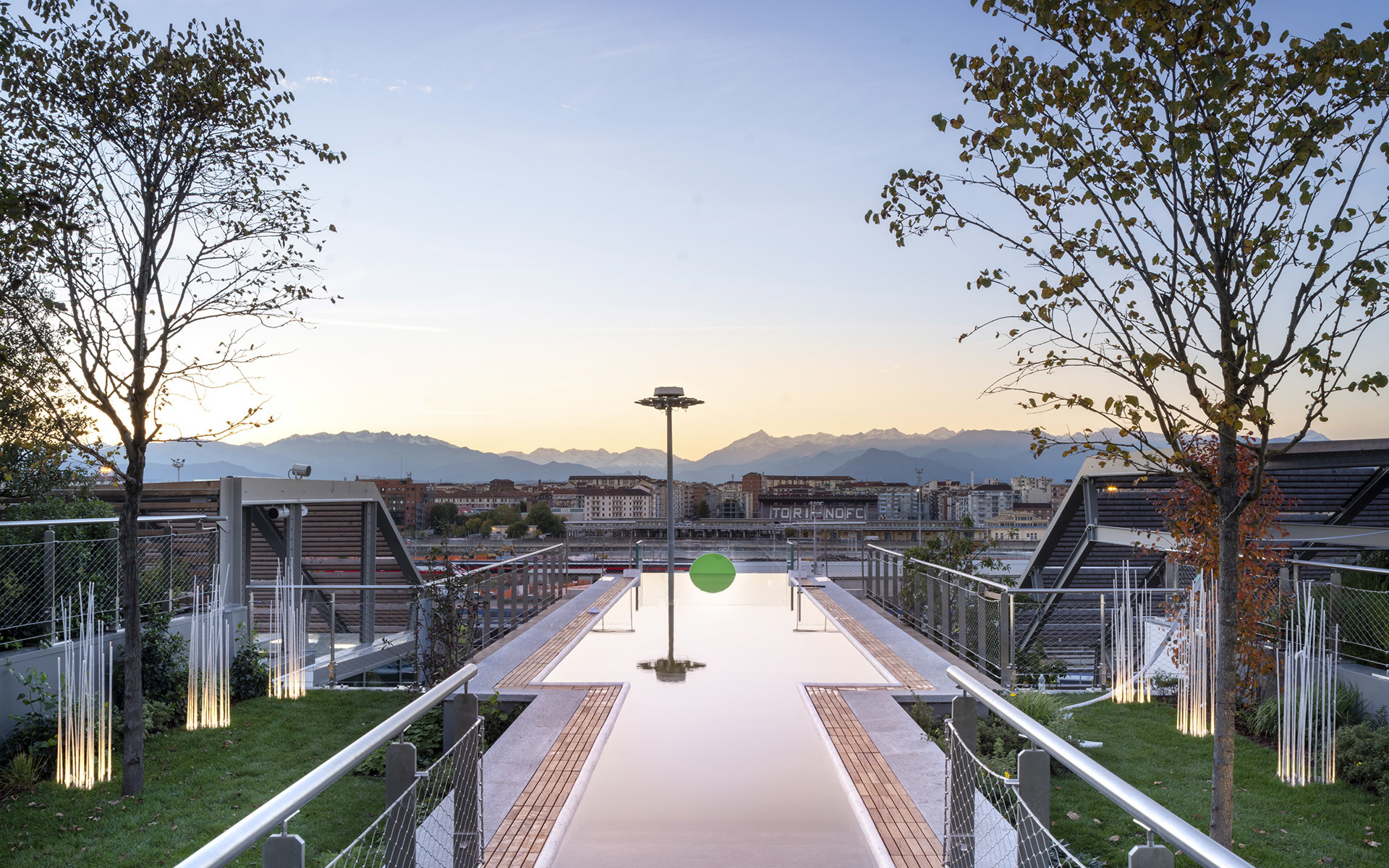 Terrazza sul tetto al crepuscolo con vasca riflettente, luci outdoor Artemide, verde rigoglioso e panorama montano sullo sfondo